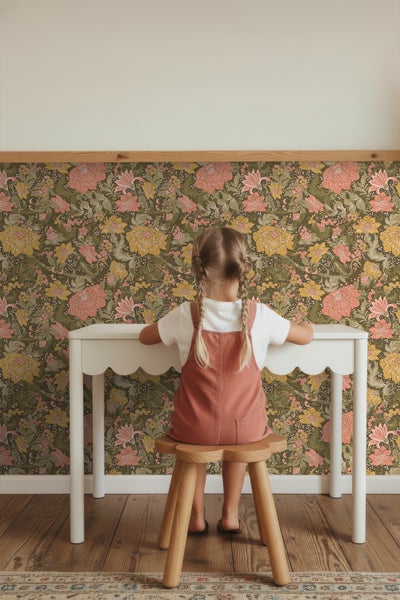 Mädchen sitzt an weißem Schreibtisch vor floraler Tapete