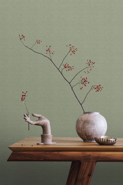 Dekorative Szene mit einer Handskulptur, einer Vase mit Zweigen und einer kleinen Schale auf einem Holztisch.