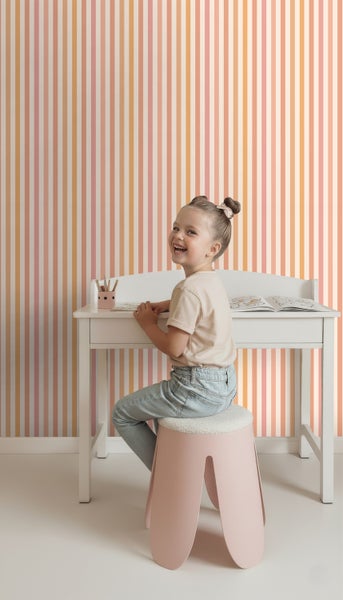 Mädchen am Schreibtisch mit gestreifter Tapete im Hintergrund