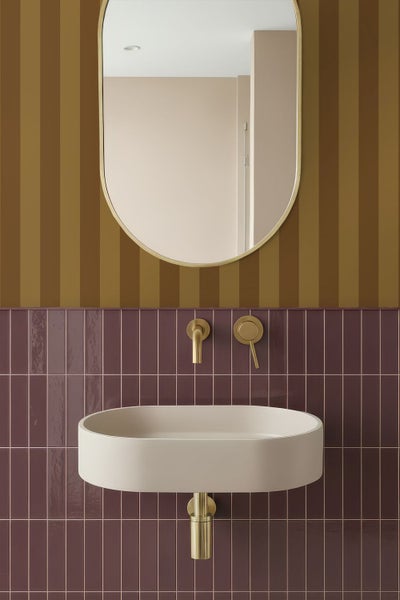 Modernes Badezimmer mit beigem Aufsatzwaschbecken, goldfarbener Unterputz-Armatur, ovalem Spiegel und vertikal verlegten Wandfliesen.