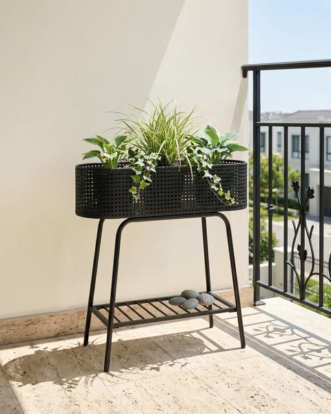 Heller Balkon mit einem schwarzen Pflanzenständer aus Metall. Der Ständer hat einen ovalen Korb in Geflechtoptik und eine untere Ablage.