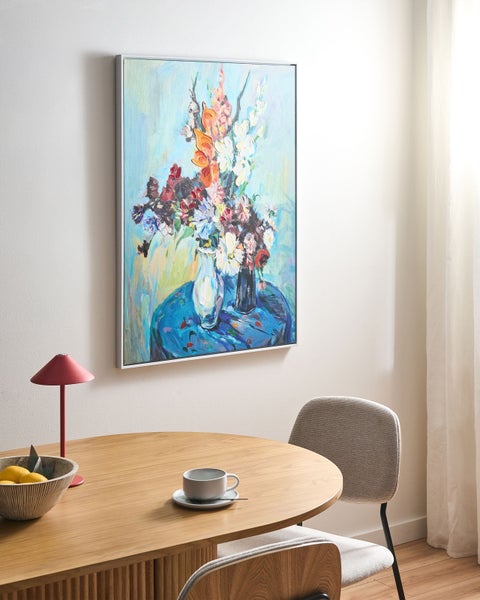 Abstraktes Leinwandbild mit Blumenstrauß in Silberrahmen über einem runden Holztisch mit Stuhl und Lampe in einem hellen, modernen Raum.