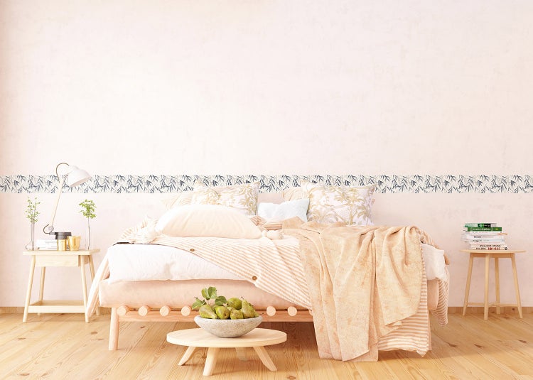 Hell gestaltetes Schlafzimmer mit Holzbett, gestreifter Bettwäsche, Holzbeistelltischen und einer Tapetenbordüre mit Blattmuster an der Wand.