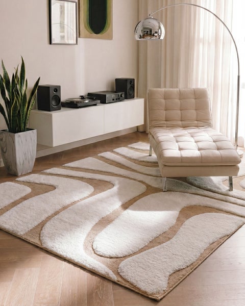Moderner Wohnbereich mit flauschigem Teppich mit Wellenmuster in Creme und Beige. Mit weißer Récamiere, Bogenleuchte und Pflanze in Marmoroptik-Topf.
