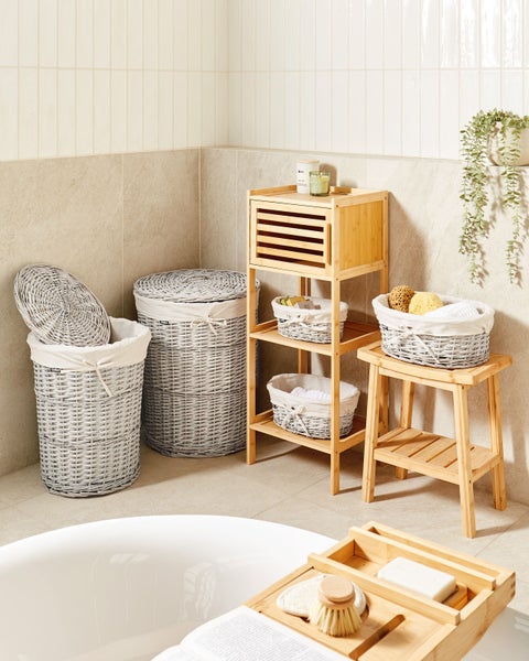 Helles, organisiertes Badezimmer mit Bambusmöbeln, darunter ein Regal und ein Hocker, sowie grauen Weidenkörben und einer Badewannenablage.