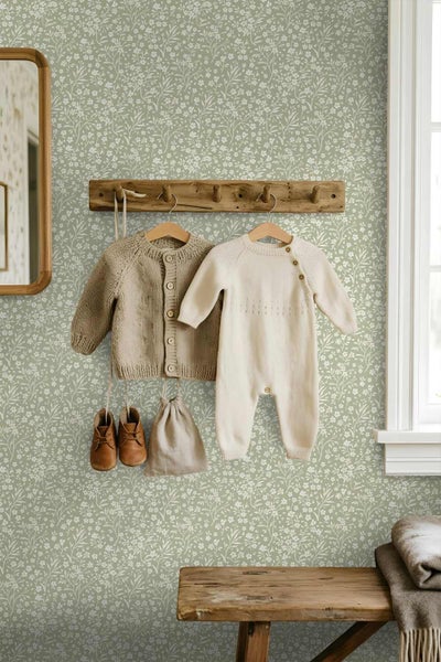 Vliestapete mit feinem weißem Blumenmuster auf grünem Grund in einem Kinderzimmer mit Holzmöbeln und hängender Babykleidung.