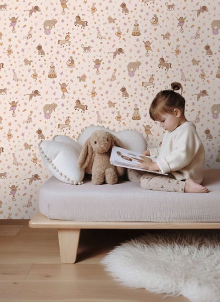 Kindertapete mit Zirkusmotiven wie Tieren und Sternen in einem hellen Kinderzimmer mit einem Kind, das auf einem Bett ein Buch liest.