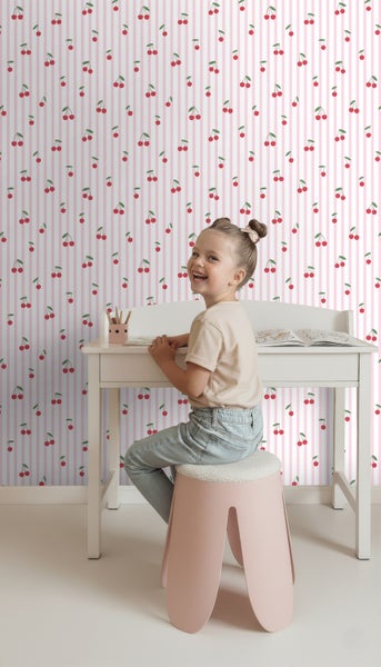 Mädchen am Schreibtisch vor gestreifter Tapete mit Kirschmuster