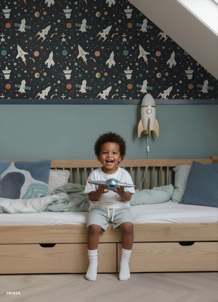 Vlies-Kindertapete mit Weltraum-Motiv aus Raketen, Planeten und Sternen in einem hellen Kinderzimmer mit Holzbett.