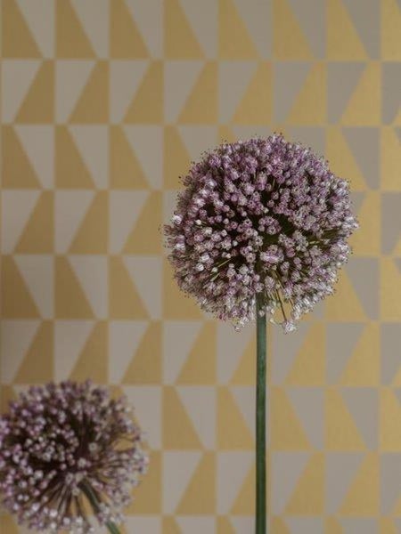 Wohnraum mit Sessel, Kommode und Lampe vor einer Wand mit geometrischem Muster