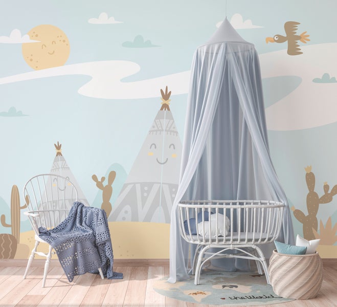 Hell eingerichtetes Kinderzimmer mit Fototapete im Wüsten-Design, weißem Babybett mit Betthimmel und Holzstuhl.