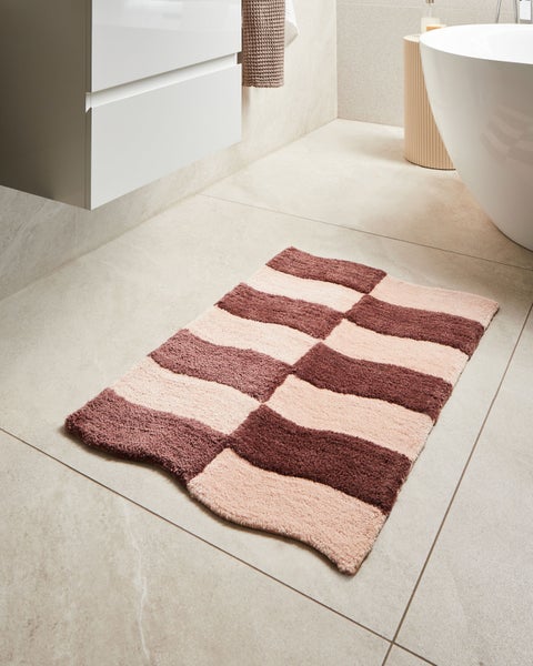 Badezimmer mit Badewanne, Waschbecken und Badteppich mit Streifenmuster