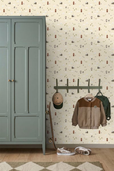 Kinderzimmer mit Mustertapete aus Häusern und Bäumen, Holzbett mit Kissen und brauner Decke, Wandregal mit Büchern und einer Holzkommode.