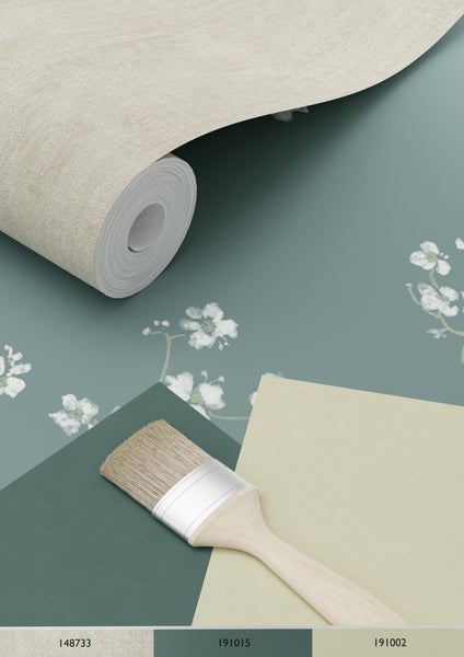 Tapetenrolle, Farbfelder und ein Pinsel auf einer Oberfläche mit Blütenmuster.
