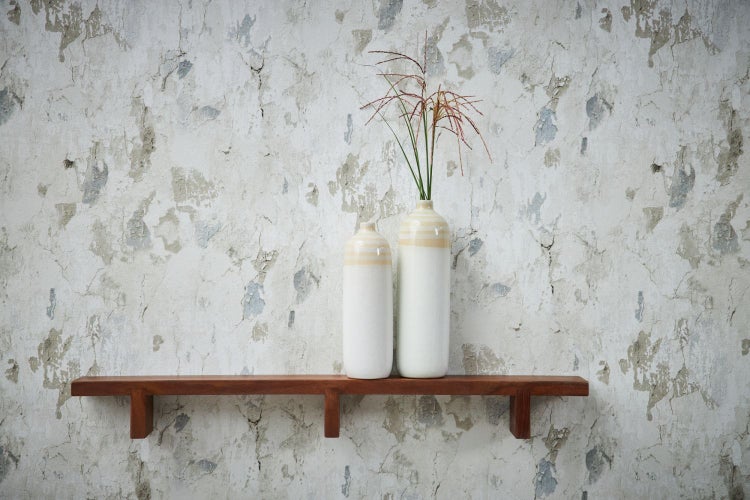 Wohnraum mit Kommode, Zimmerpflanze und Dekorationsgegenständen vor einer gemusterten Tapete.