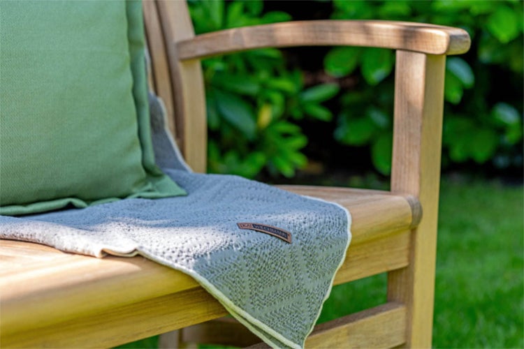 Gartenszene mit einem hölzernen Gartenstuhl mit Kissen und Decke