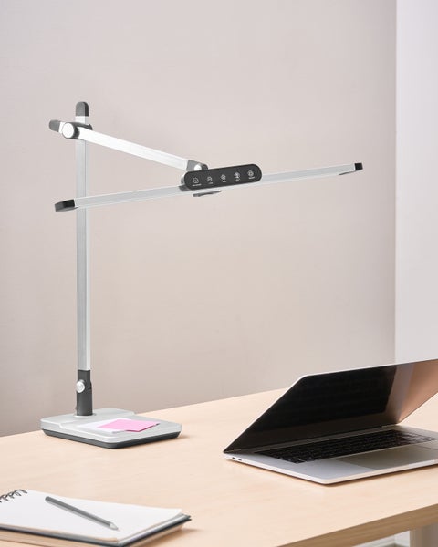 Schreibtisch mit einer LED-Tischleuchte, einem Notizblock und einem Laptop.