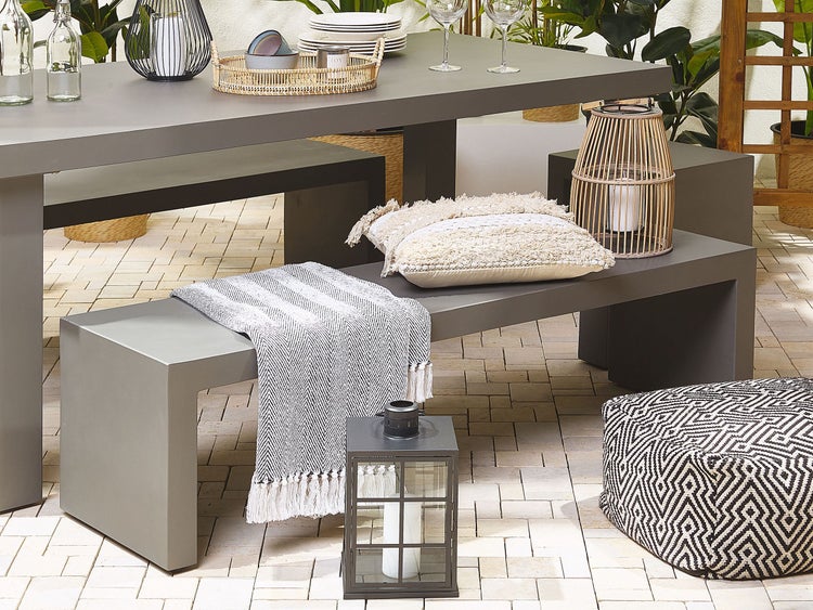 Gartenszene mit Esstisch, Bänken, Kissen, Decken, Windlichtern und Pouf für den Außenbereich