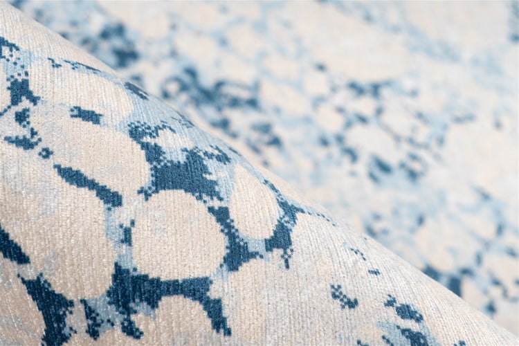 Nahaufnahme eines Teppichs mit abstraktem meliertem Muster in Blau und Beige.
