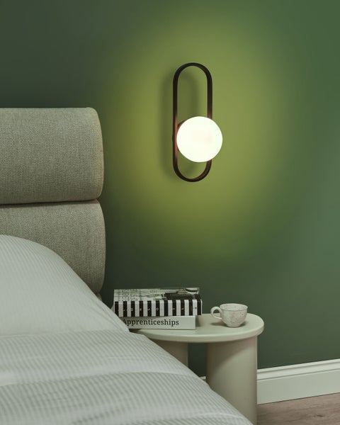 Wandleuchte mit kugelförmigem Lampenschirm neben einem Bett und einem Nachttisch