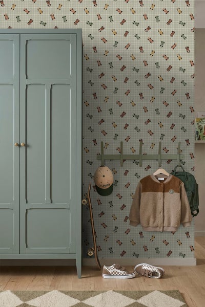Kinderzimmer mit einer Vliestapete mit Rennwagen-Muster auf Karohintergrund, daneben ein grüner Schrank und eine Garderobe.