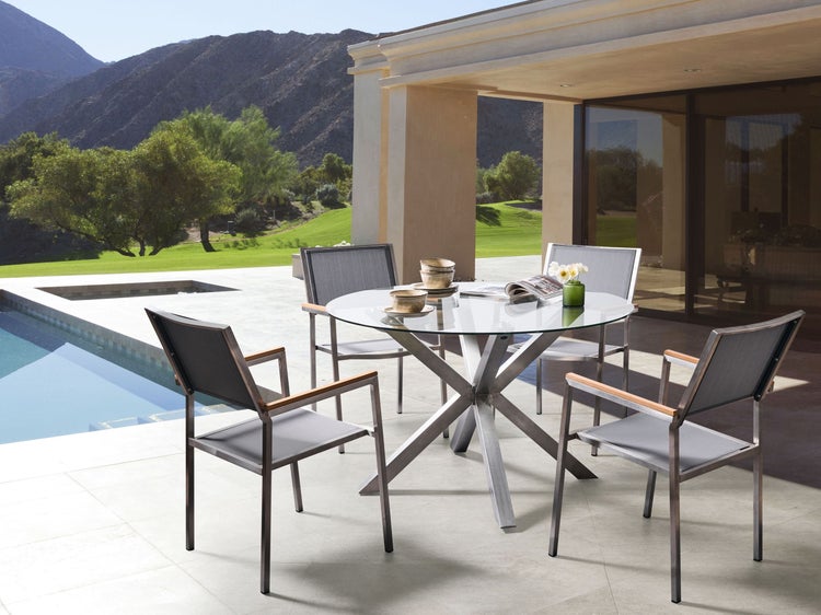 Gartenszene mit runder Glasplatte auf Metalltisch und vier Stühlen mit Textilsitzen im Außenbereich