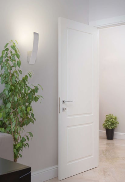 Innenraum mit geöffneter Tür, Wandleuchte und Zimmerpflanzen für ein helles Ambiente.