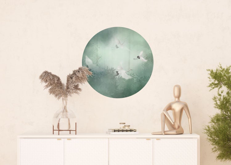 Wandgestaltung mit Kranichmotiv über einem weißen Schrank mit Dekorationen wie einer goldenen Skulptur, Büchern und einer Vase mit getrockneten Pflanzen