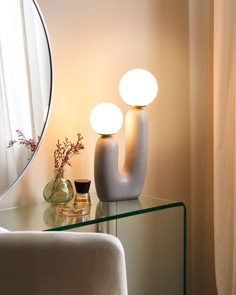 Dekoratives Arrangement mit Tischleuchte, Spiegel und Accessoires auf einem Glasregal.