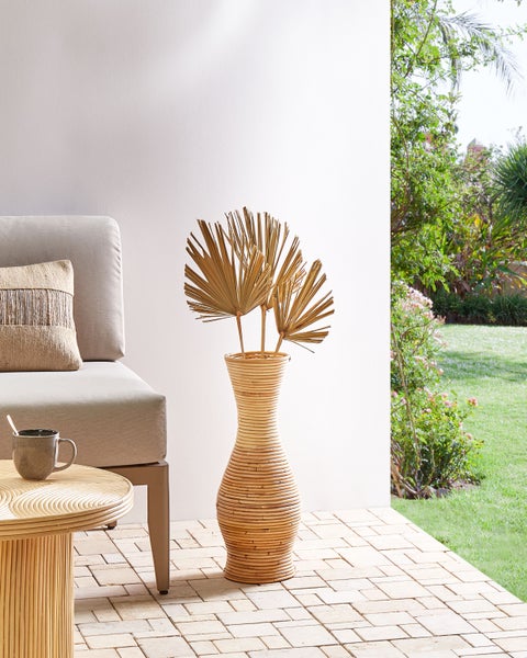 Szene mit Rattanvase, Fächerpalmen, Couch, Kaffeetasse und Beistelltisch im Freien