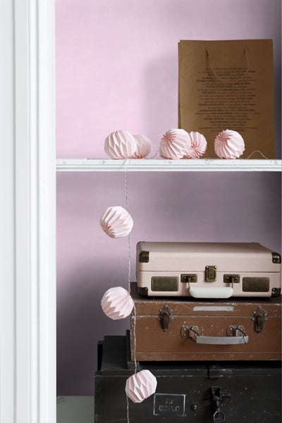 Dekoratives Regal mit Reisekoffern, Papiertüte und Papierkugeln als Lichterkette