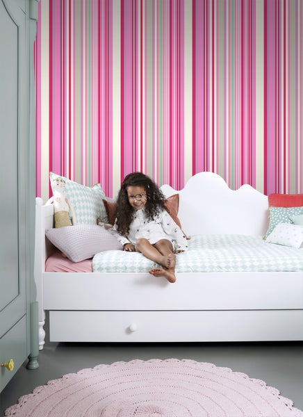 Zimmer mit gestreifter Tapete, Mädchen auf einem Tagesbett, Schrank und rundem Teppich.