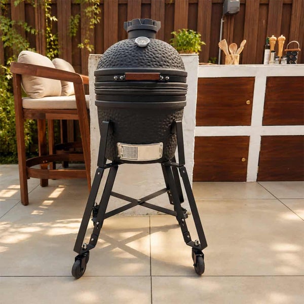 Keramikgrill Kamado auf einem rollbaren Metallgestell, stehend auf einer Terrasse mit Außenküche.