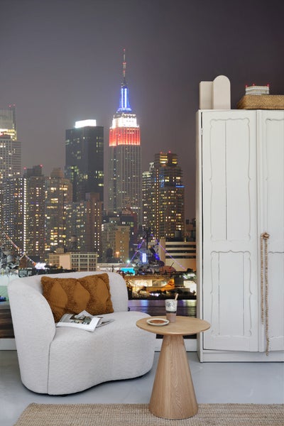 Wohnraum mit Sessel, Beistelltisch und Schrank vor einer New Yorker Skyline Tapete.