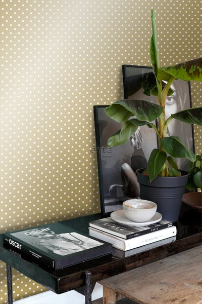 Dekorative Szene mit Tapete mit Punktmuster, gerahmten Bildern, Zimmerpflanze und Büchern