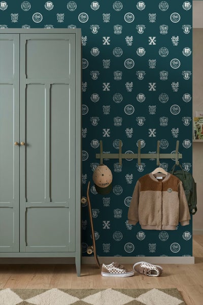 Dunkelgrüne Tapete mit College-Wappen und Schriftzügen in einem Kinderzimmer mit grünem Kleiderschrank, Garderobenleiste, Jacke und Skateboard.
