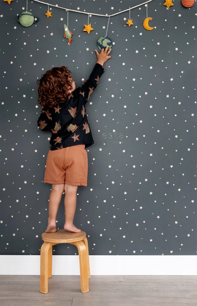 Junge auf Hocker vor Wand mit Sternen-Tapete und Weltraum-Dekoration