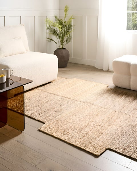 Strukturierter beige Teppich aus rechteckigen Elementen in hellem Wohnzimmer mit Bouclé-Sofa, Palme und Glasbeistelltisch.