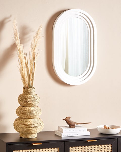 Dekoratives Interieur mit Spiegel, Vase mit Pampasgras, Holzfigur und Schale auf einer Kommode