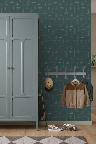Vliestapete mit Segelboot-Motiven in einem Kinderzimmer neben einem Kleiderschrank, einer Garderobe und einem Skateboard.