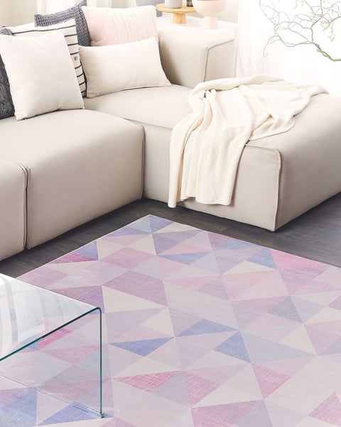 Moderner Wohnraum mit einem geometrisch gemusterten Teppich auf dunklem Holzboden, einem hellen Ecksofa mit Kissen und einem Glastisch.