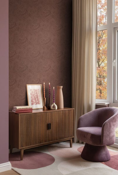 Wohnzimmer mit brauner gemusterter Tapete, Holzkommode, Dekoration und lila Sessel