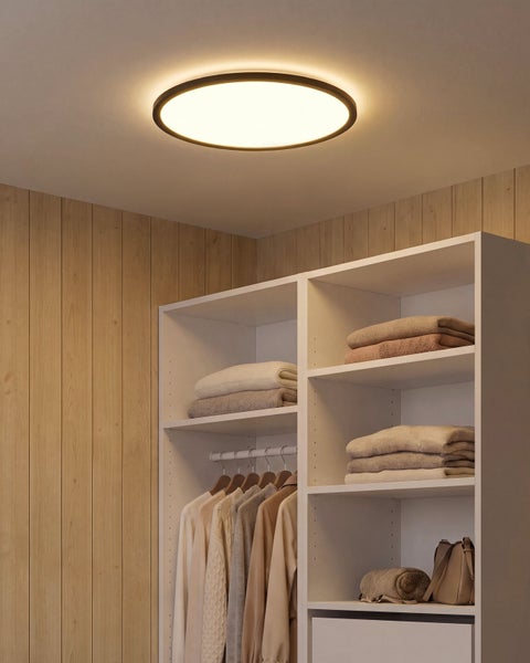 Runde LED Deckenleuchte in einem Ankleidezimmer mit Holzpaneelen und weißem Kleiderschrank mit Kleidung und Accessoires.