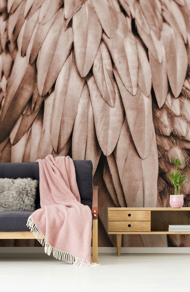 Fototapete mit Nahaufnahme von Federn in einem Wohnzimmer mit dunklem Sofa, rosa Decke und hellem Sideboard aus Holz.