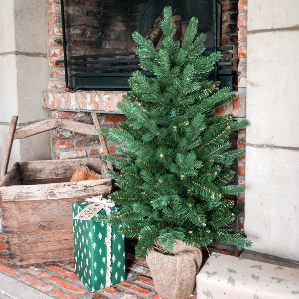 Künstlicher Weihnachtsbaum neben einem Kamin mit Geschenken in einer Wohnzimmerszene