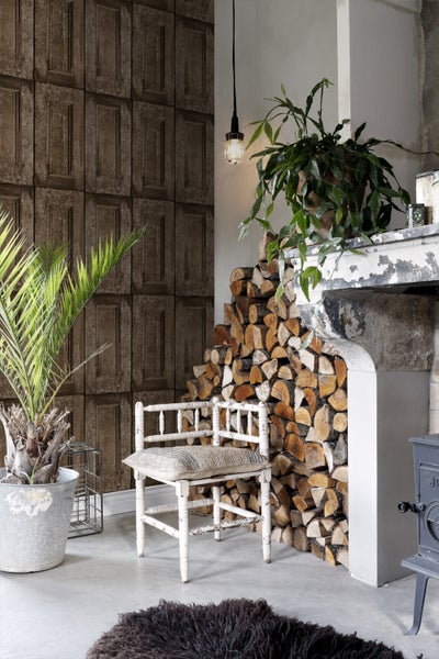 Wohnraum mit Kaminholz, Zimmerpflanzen und einer Wand mit Holzpaneel-Tapete