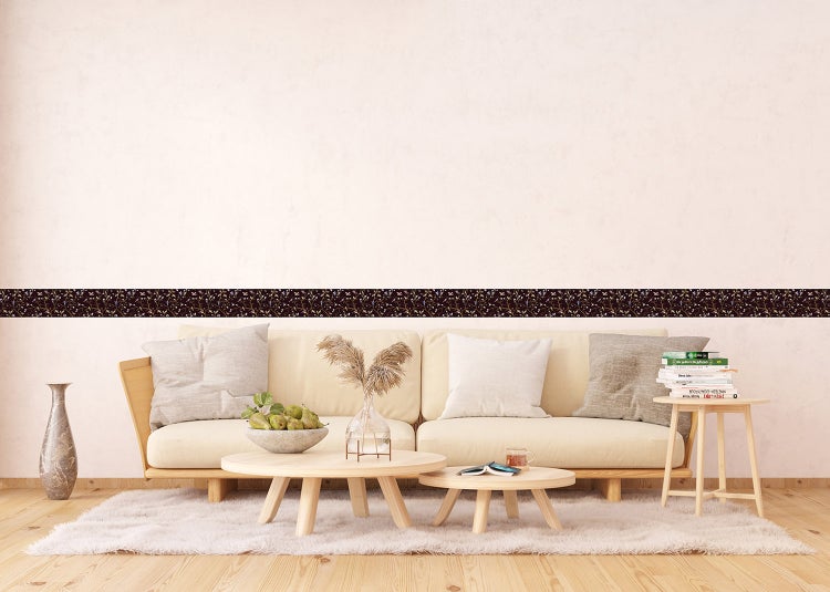 Tapetenbordüre mit floralem Muster auf dunklem Grund in einem hellen Wohnzimmer mit Sofa und Holztischen.