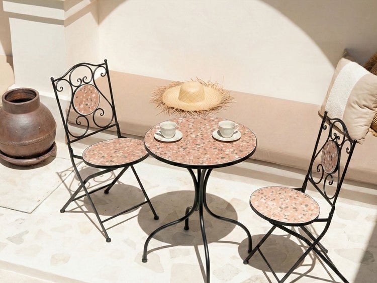 Szene mit Gartentisch und zwei Stühlen aus Metall mit Terrazzo-Optik, zwei Kaffeetassen und einem Strohhut