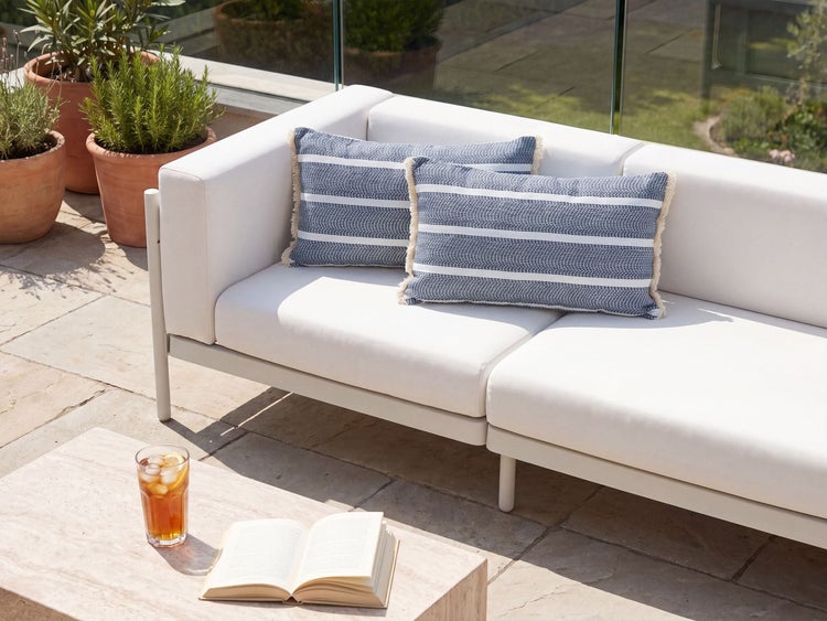 Gartenlounge mit zwei gestreiften Zierkissen auf einer Terrasse mit Steintisch und Topfpflanzen.