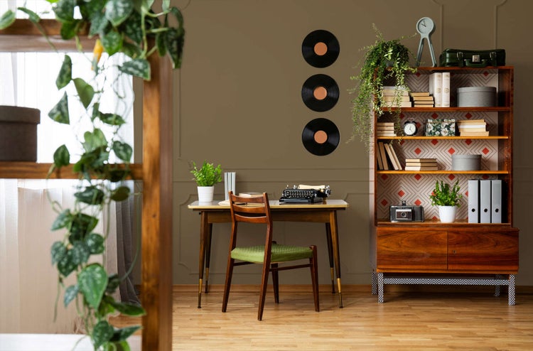 Retro-Arbeitszimmer mit olivbrauner Wandfarbe, Holzschreibtisch, Schreibmaschine, Holzregal und Schallplatten auf hellem Parkettboden.